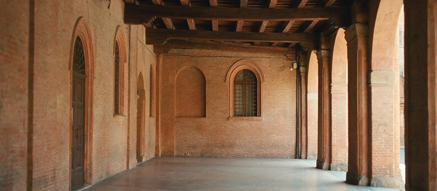 Un portico con arcate in mattoni rossi e soffitto di travi in legno, vuoto, nella luce del pomeriggio