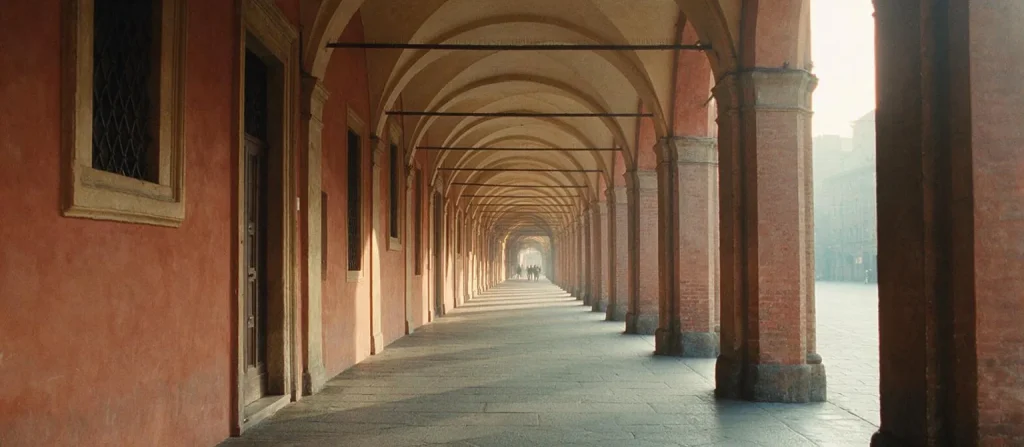 Un lungo portico con arcate e pareti in mattoni rossi in prospettiva, nella luce del mattino